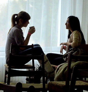 Decorative: two women, in their 20s, sitting in a casual manner, talking and drinking coffee.